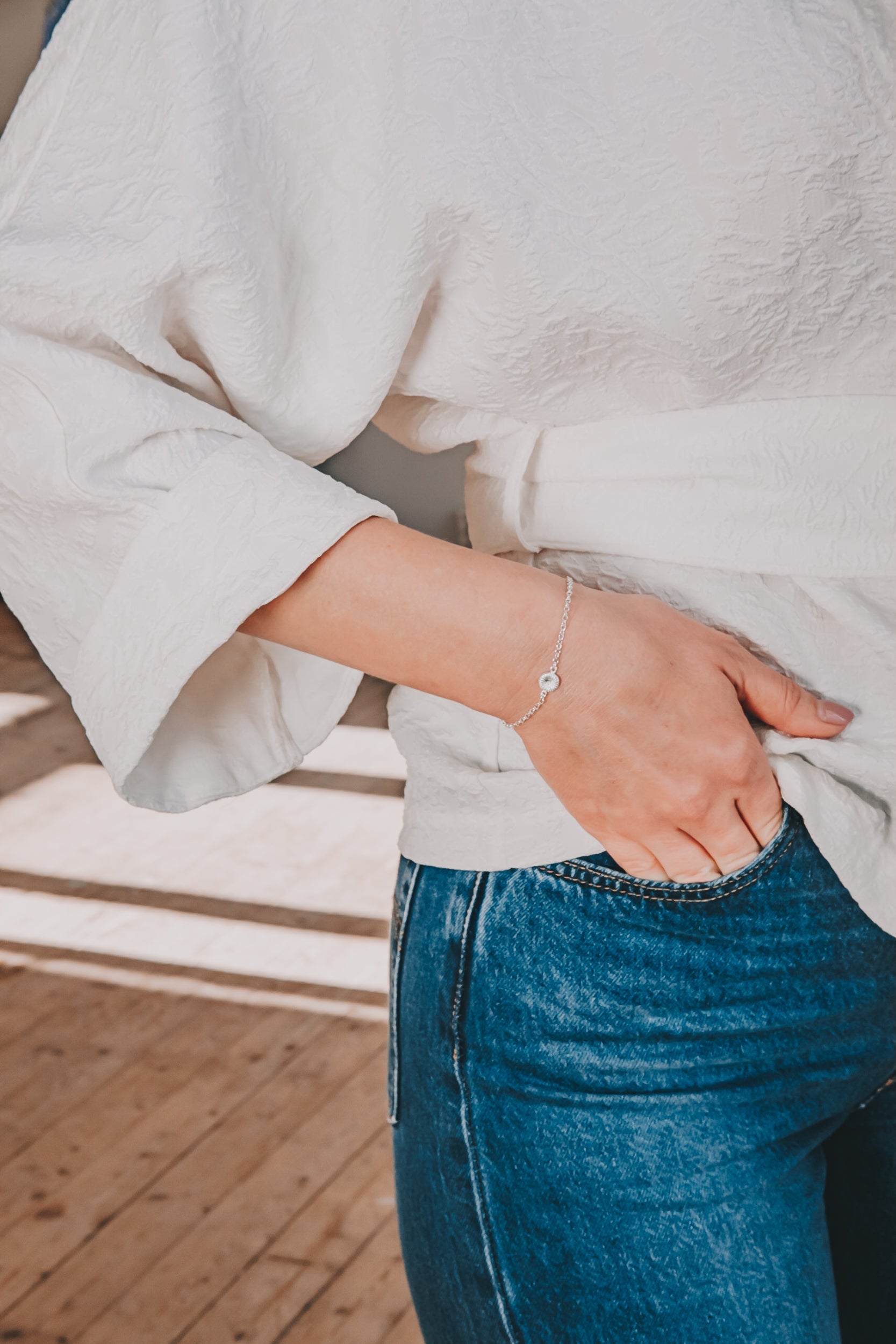 Jag vet inte vem personen är, men bilden visar en person i en vit blus och blå jeans som bär ett elegant armband.