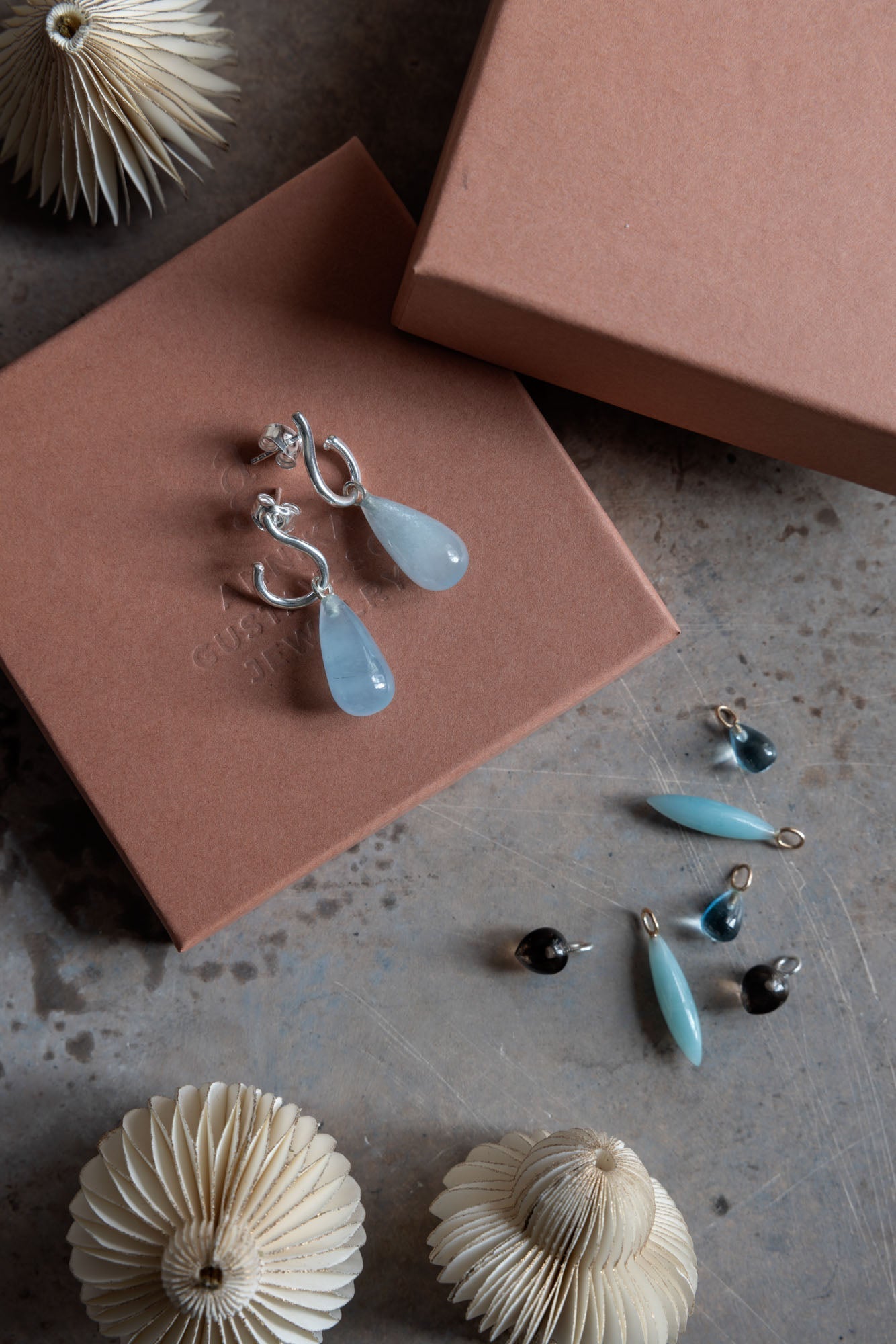 Elegant örhängen och hängen i blå toner på betongyta.